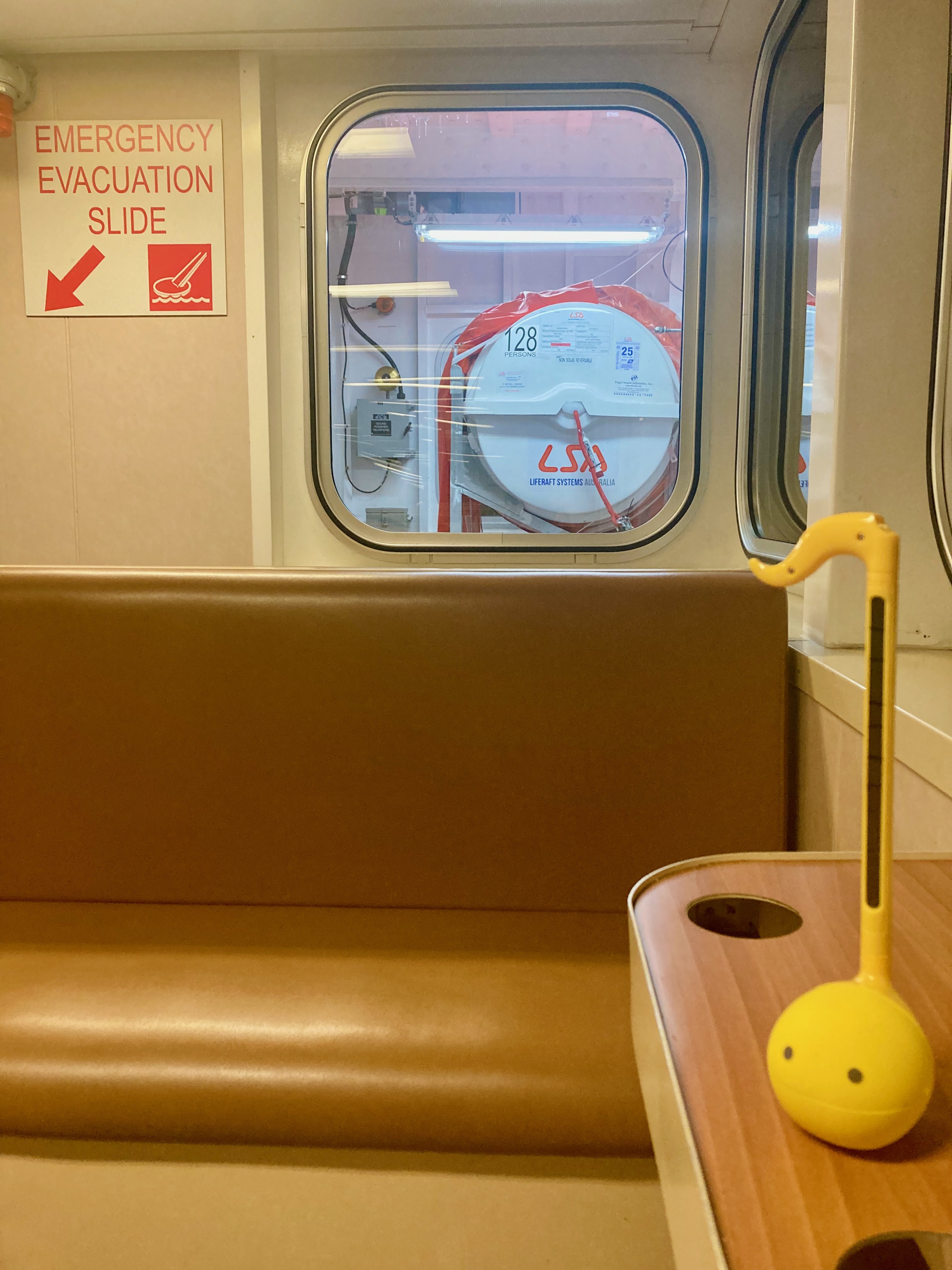 photo of a yellow otamatone sitting on an empty seat inside a ferry